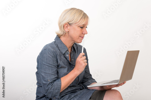 beautiful european mid aged woman working at a laptop thoughtful - studio shot in front of light background
