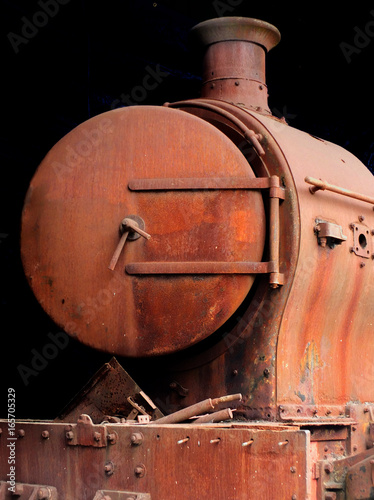 old rusting abandoned steam locomotive from the front showing door buffers and chimney on a black background photo