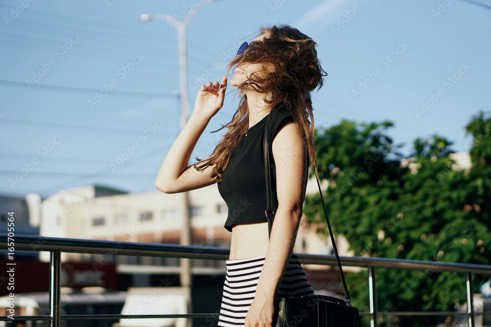Young beautiful woman in sunglasses walking along the street in the city, the wind