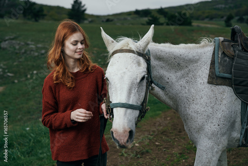 Young beautiful woman is walking with a white horse in the mountains
