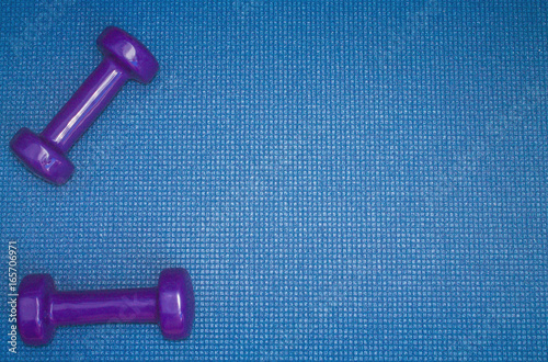 Blue background. Mat for sport, yoga and meditation. Two purple dumbbells. photo
