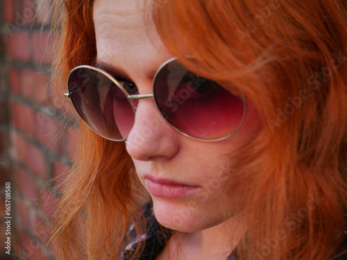 cute red haired girl with glasses against brick wall