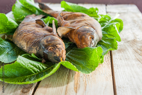 The smoked baked fish is laid out on green leaves lying on coarse unglued boards. Home healthy eating at a picnic photo