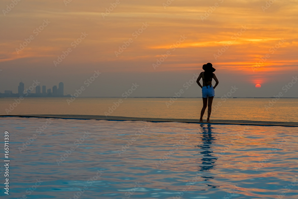 Young woman happy in big hat relaxing on the swimming pool, travel near the sea and beach in the sunset. Summer Concept