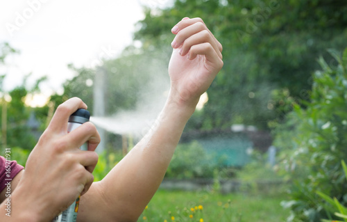 Young man spraying mosquito / insect repellent in the forrest, insect protection photo