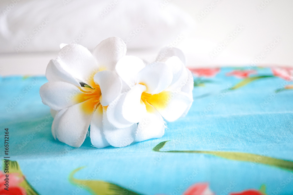 Bali dress (in blue with flower pattern) and artificial plumeria flower crown on the bed. Concept of summer vacation. Hotel complimentary, room in a hotel. Soft window light.