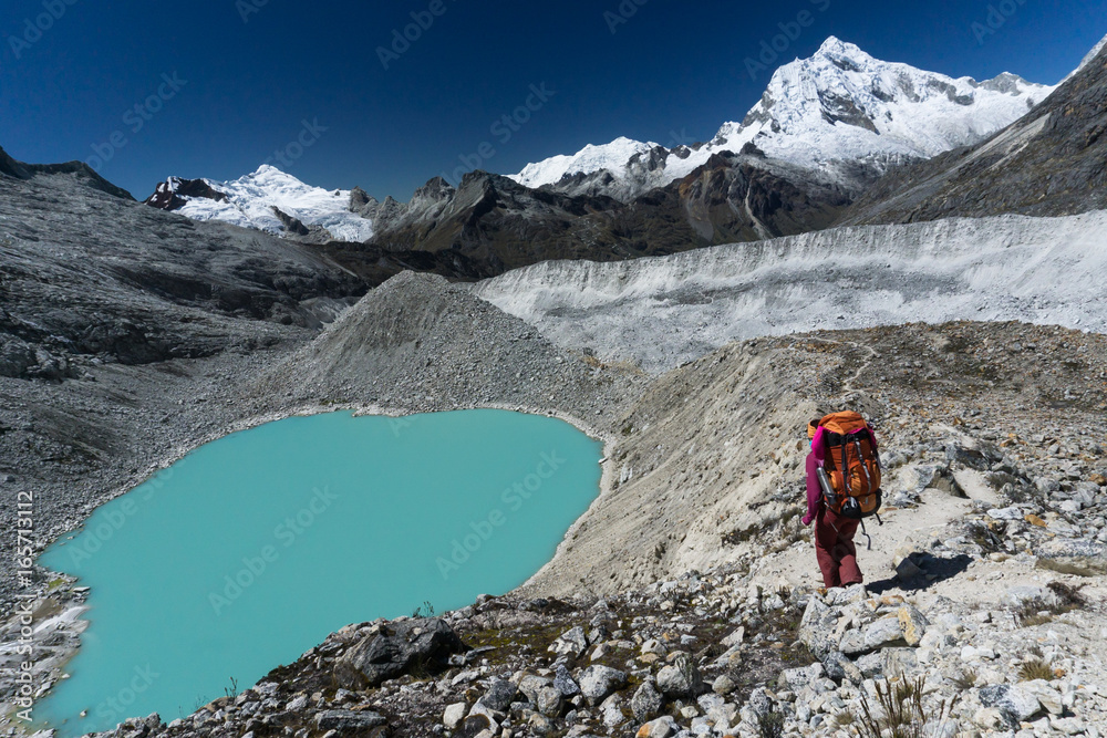 single female mountain climber with large backpack near a turquoise mountain lake while descending from a high altitude peak in the Cordillera Blanca in the Andes in Peru