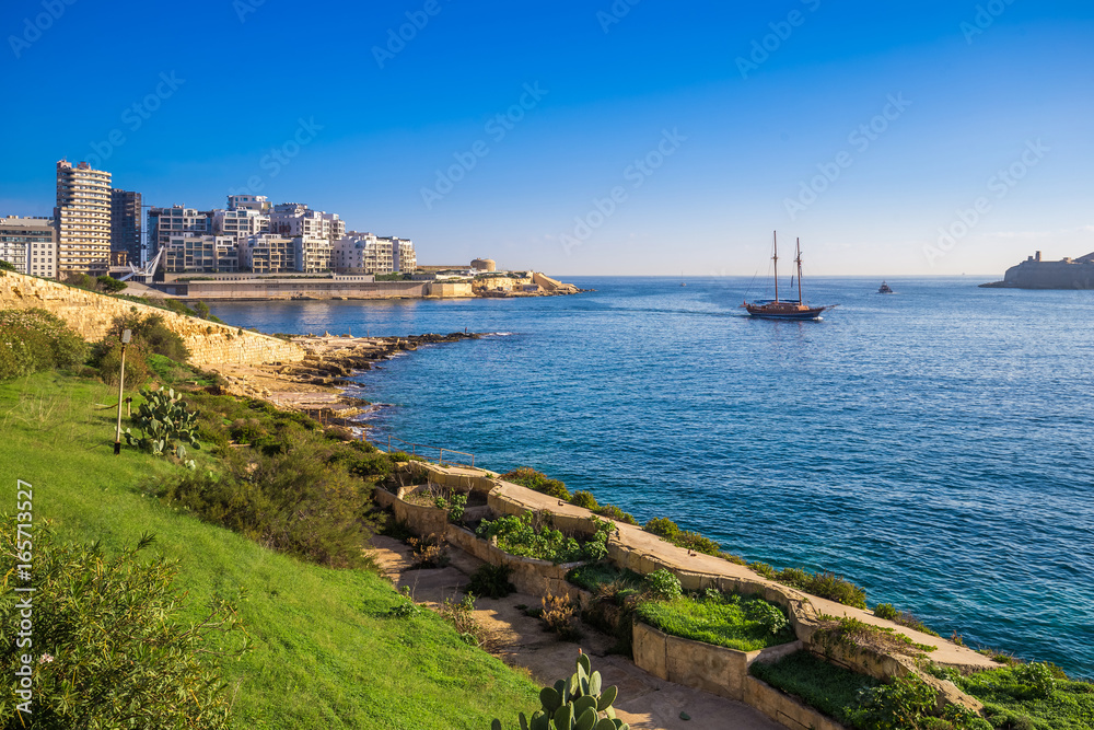 Valletta, Malta - Skyline view of Sliema at sunrise shot from Manoel island at spring time with sailing boat, blue sky and green grass