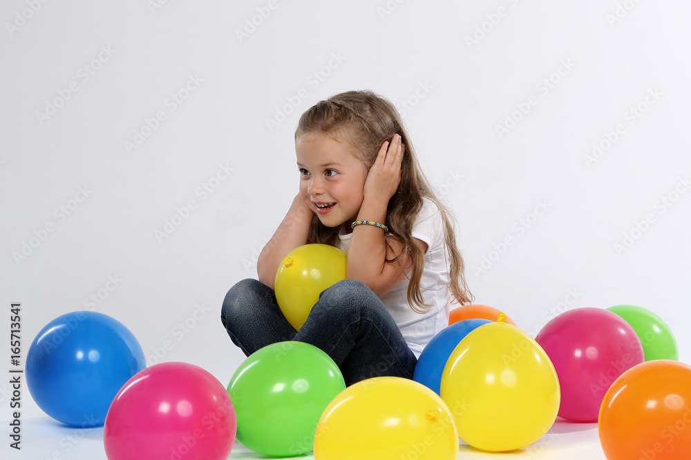 Kleines Mädchen sitzt zwischen Ballons und hält sich die Ohren zu Stock  Photo | Adobe Stock