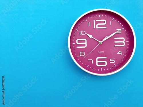 Closeup A pink wall clock set on blue background . Top view with Copy space. Selective focus.