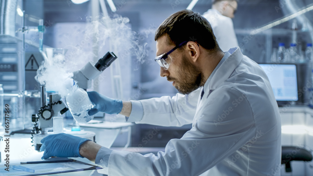 In a Secure High Level Laboratory Scientists in a Coverall Conducting a Research. Chemist Adjusts Samples in a Petri Dish with Pincers. In a Secure High Level Laboratory Scientists in a Coverall Conducting a Research. Chemist Adjusts Samples in a Petri Dish with Pincers.