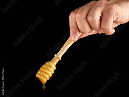 Hand holding Wooden dipper for honey isolated on black