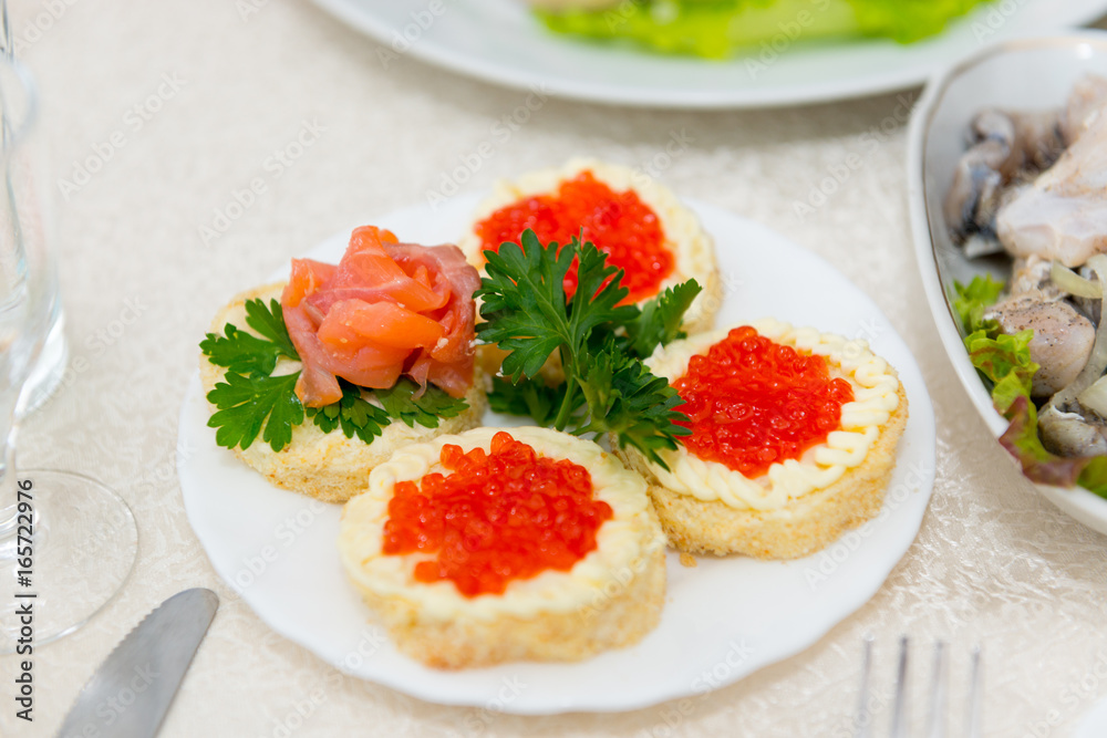 Sandwiches with red caviar and salmon are spread on a plate on a buffet table close up. Sandwiches with red caviar and salmon are spread on a plate on a buffet table close up.