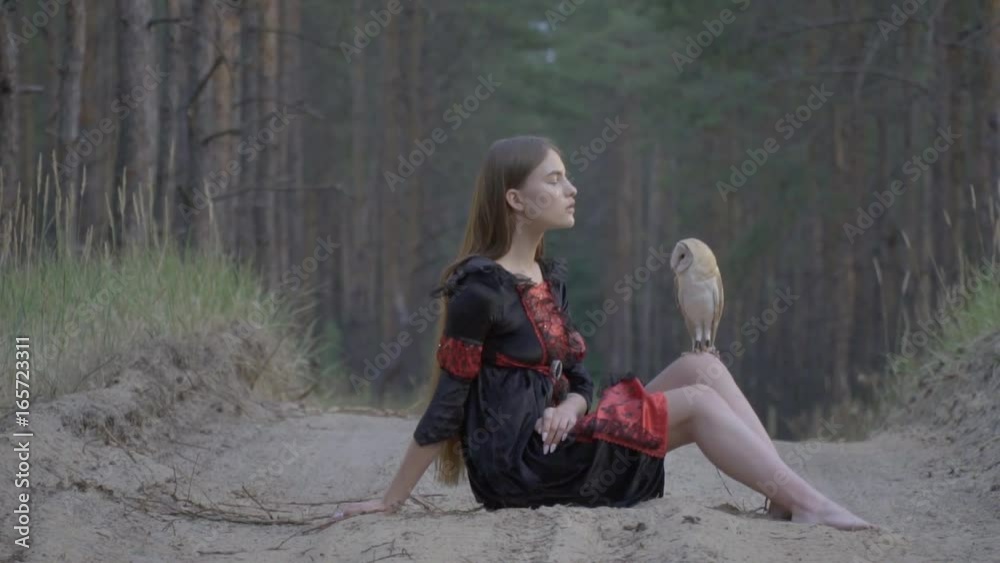 A girl with long hair in a black dress is sitting barefoot on a ...