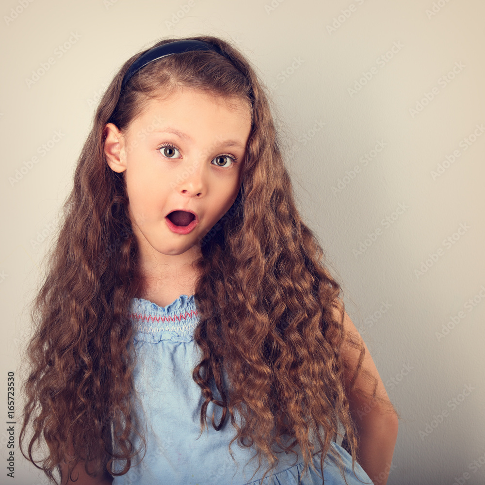 Excited surprising kid girl with long curly hair style and wide open mouth  and big eyes looking. Toned portrait Stock Photo | Adobe Stock