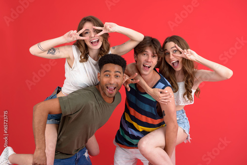Happy group of friends standing isolated over red background © Drobot Dean