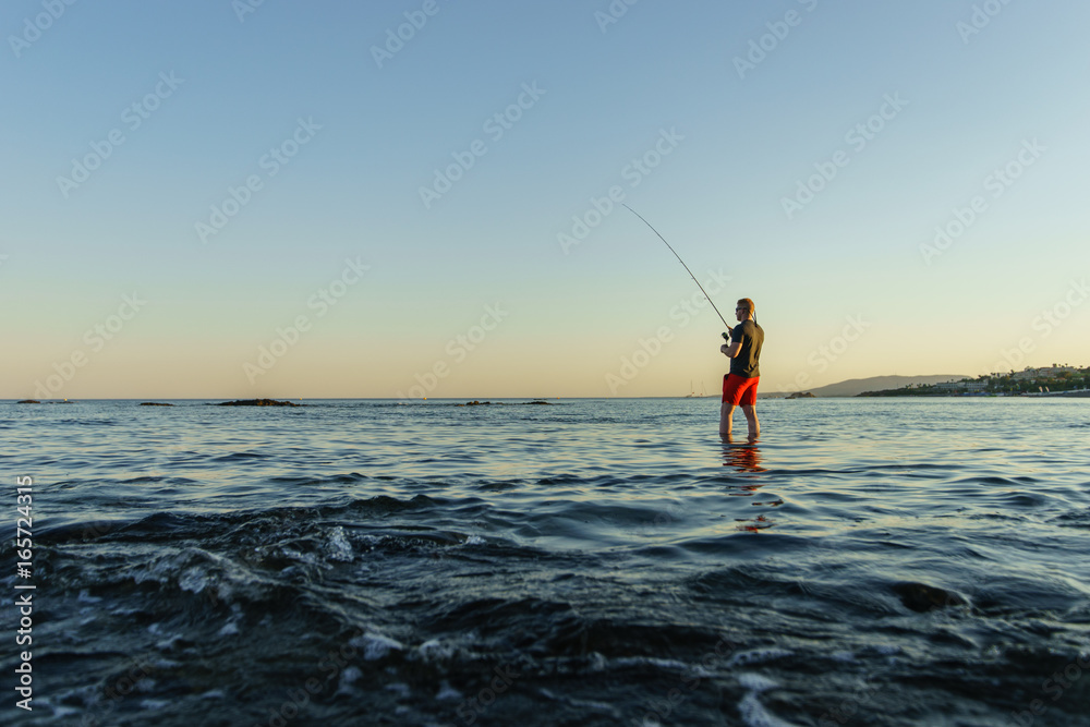 Angler angelt im Meer bei Sonnenuntergang