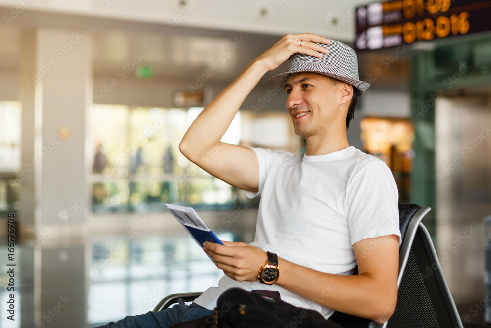 A man in a hat holding passport and boarding pass at airport