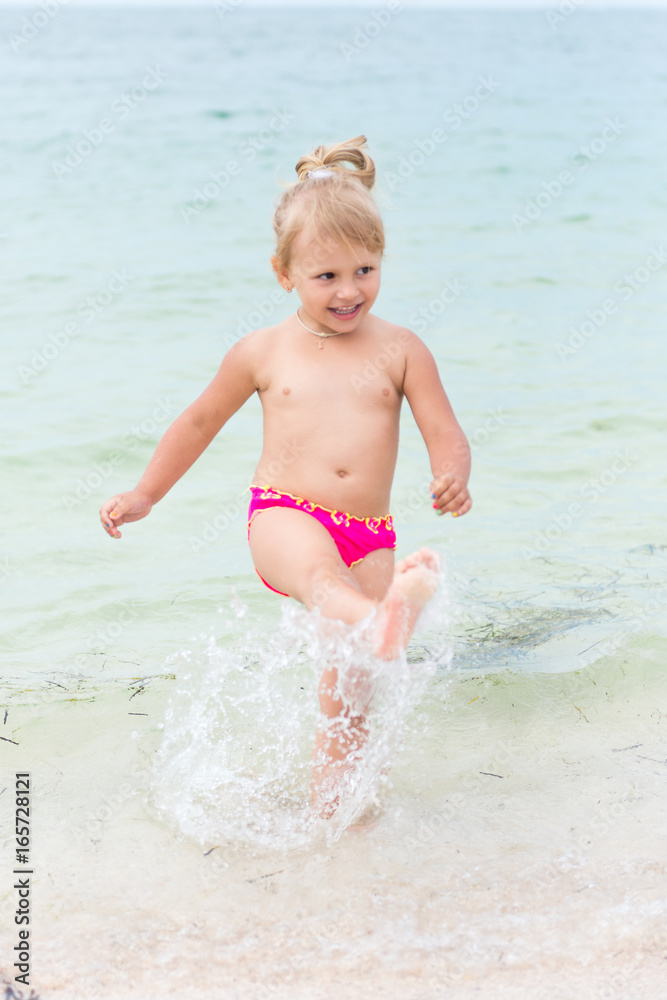 Little girl playing in the waves at sea on a sunny day. Carefree childhood on the sea beach. Little girl playing in the waves at sea on a sunny day. Carefree childhood on the sea beach.