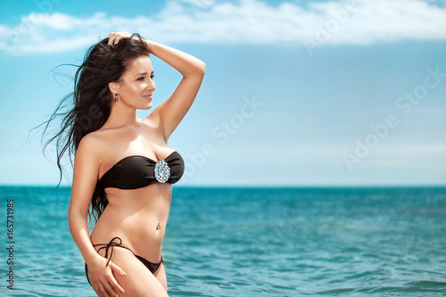 Overweight young woman in black swimsuit near the sea. Size plus or king size woman. Summer photo with copy space
