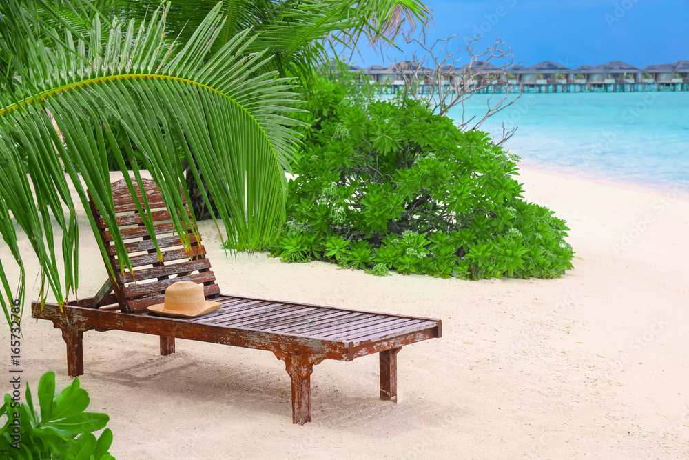Wooden sun lounger with hat on tropical beach