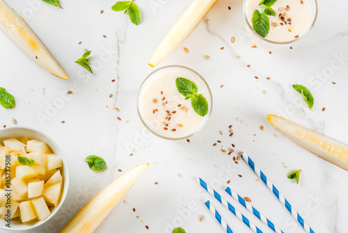 Summer fruits, refreshing drinks. Vegan food. Breakfast. Smoothie of yogurt, raw organic yellow melon, flax seeds and mint. With striped straws, in glasses, white marble table, copy space  top view photo