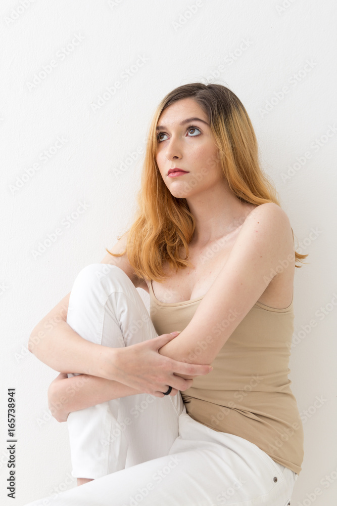 Beautiful blonde teen girl looking up is sitting with one of her legs bent. Beautiful blonde teen girl looking up is sitting with one of her legs bent.