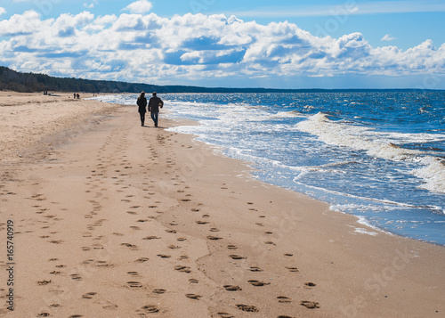 Couple is walking along the beach under blue sky