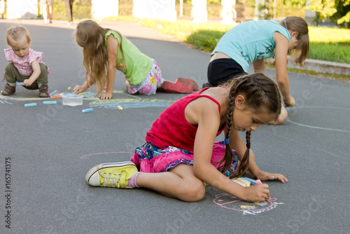 Kids absorbedly draw chalks on the pavement