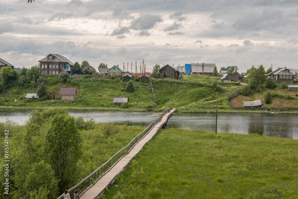 north Russian village Isady. Summer day, Emca river, old cottages on the shore, old wooden bridge and clouds reflections. north Russian village Isady. Summer day, Emca river, old cottages on the shore, old wooden bridge and clouds reflections.