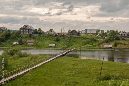 north Russian village Isady. Summer day, Emca river, old cottages on the shore, old wooden bridge and clouds reflections. photo