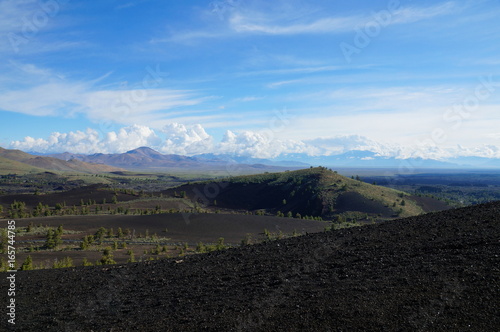 View over a black volcanic lava landscape from the Inferno Cone. A cinder cone rising above a landscape of black volcanic basalt rock and volcano domes from eruptions. Craters of the Moon.