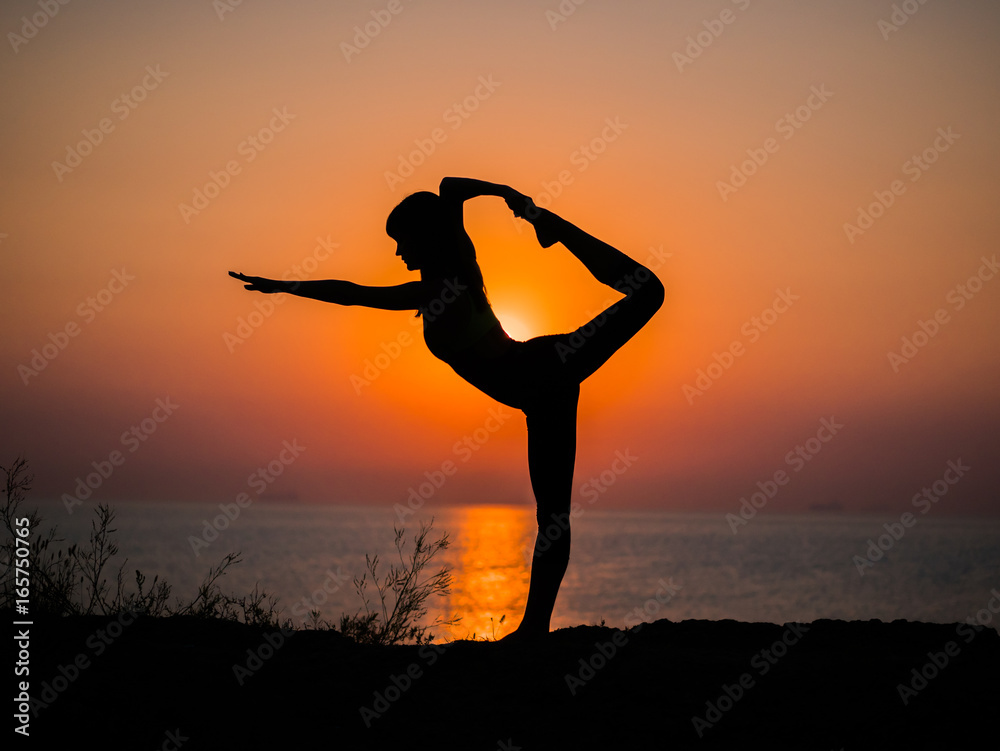 Silhouette young woman practicing yoga on the beach above sea at amazing sunset. fitness, sport, yoga and healthy lifestyle concept.