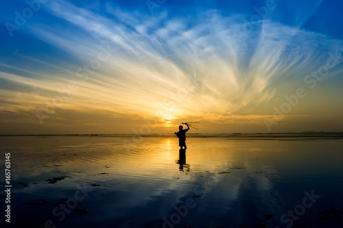 Minimal Silhouette of happy tourist with poles in hand above head on the beach with sunrise sky. © noppharat