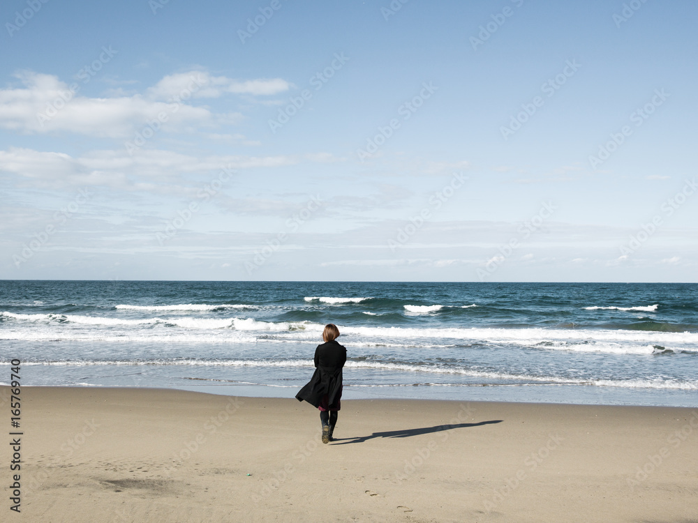 A woman walking towards the sea A woman walking towards the sea