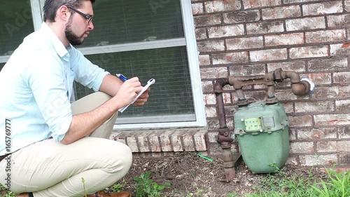 Young millennial home inspector examines gas meter outside a residential home photo