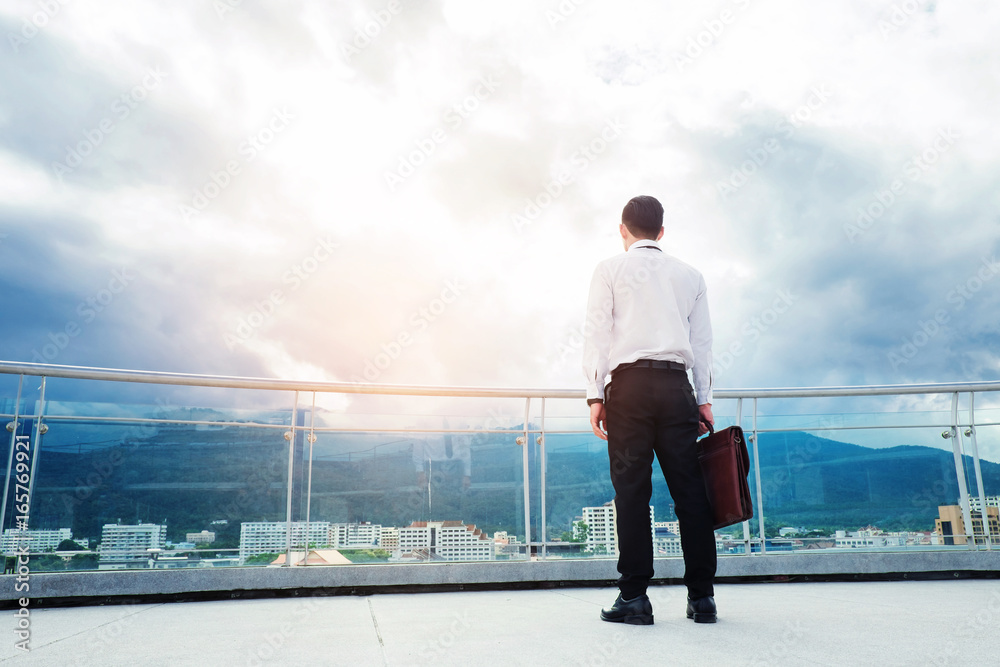 Businessman standing on a roof and looking at city Success and thinking concept