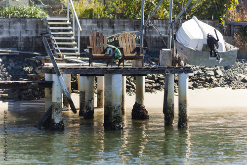 Deteriorating jetty with old timber chairs and dingy at low tide photo