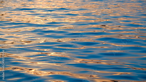Gold and blue shimmering surface of a water during the sunrise, Sea wave close up, low angle view good for the backgrounds and wallpapers