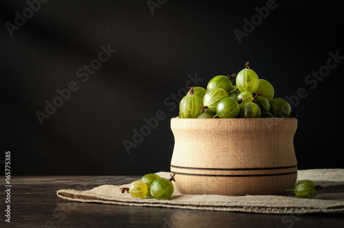 Juicy ripe berries of a gooseberry in a small wooden pot on black surface. Gooseberry harvest