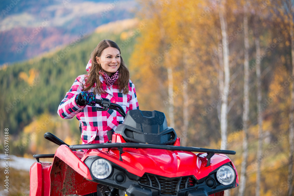 Close-up portait of happy girl in winter clothing on red quad bike in the autumn nature