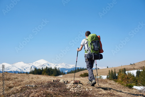 Rearview low angle shot of an adventurous man wearing backpack using hiking sticks while walking the mountain copyspace travelling adventure nature landscape sport activity