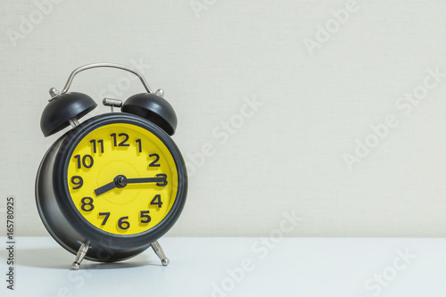 Closeup yellow and black alarm clock for decorate show a quarter past eight o'clock or 8:15 a.m.on white wood desk and cream wallpaper textured background tone with copy space