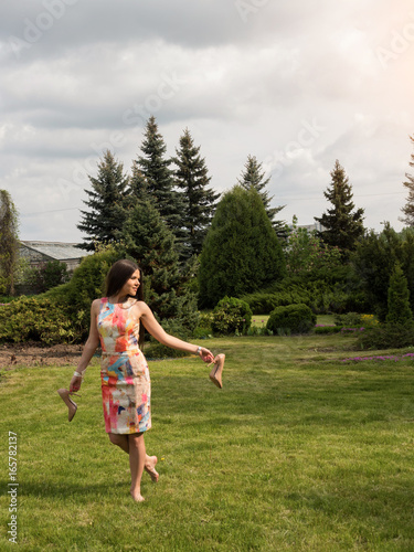 The girl holds shoes in her hands and walks barefoot on the grass. Rest for feet