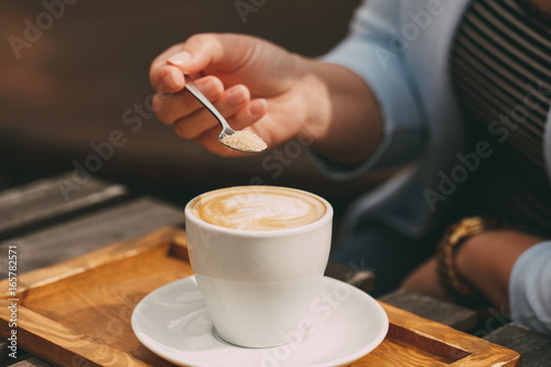 Close-up of a spoon in a female hand pouring sugar into her coffee cup