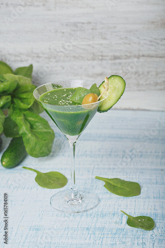 Green spinach and cucumber smoothie on light blue wooden background.