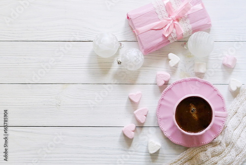 Pink cup with coffee, marshmallows hearts, Christmas balls and gift on a white wooden background.Top view. Copy space
