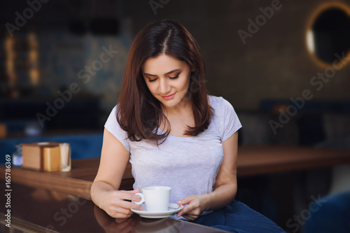 Smiling woman in a good mood with cup of coffee sitting in cafe.