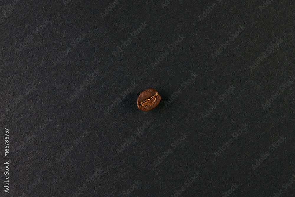 Top view of a one shiny fresh roasted coffee bean isolated on dark stone background. Top view of a one shiny fresh roasted coffee bean isolated on dark stone background.