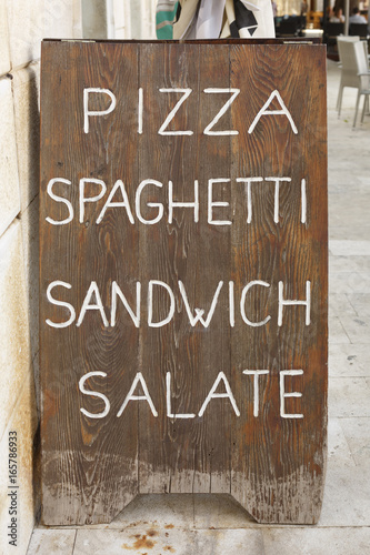 Handwritten sign on wooden board, Sign for pizza, spaghetti, sandwiches and salads written in white letters